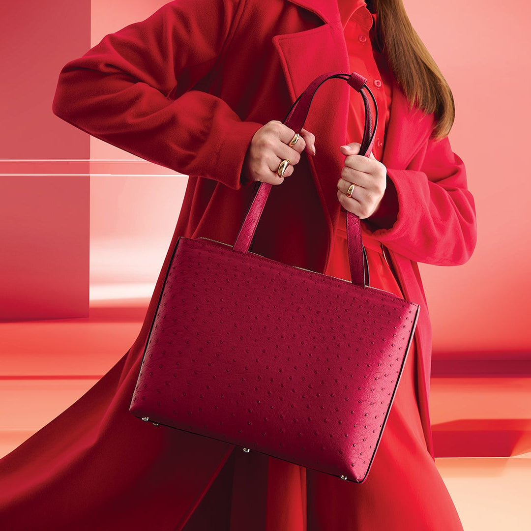 Person wearing a red coat holding a matching red handbag against a red background