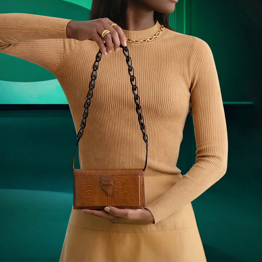 Woman holding a brown handbag with a chain strap against a teal background