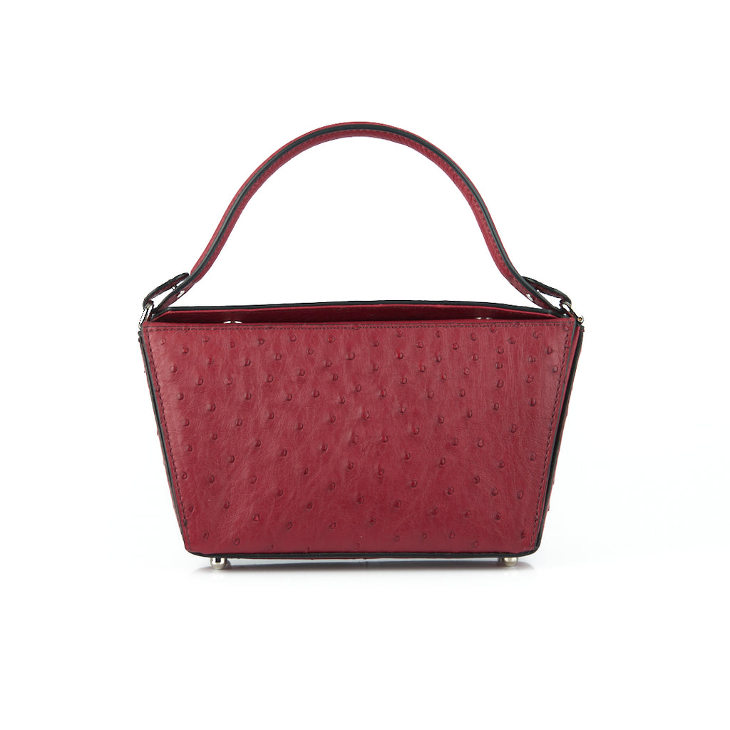 A red leather handbag with a structured handle and a detachable strap, featuring a textured exterior and a sleek design.