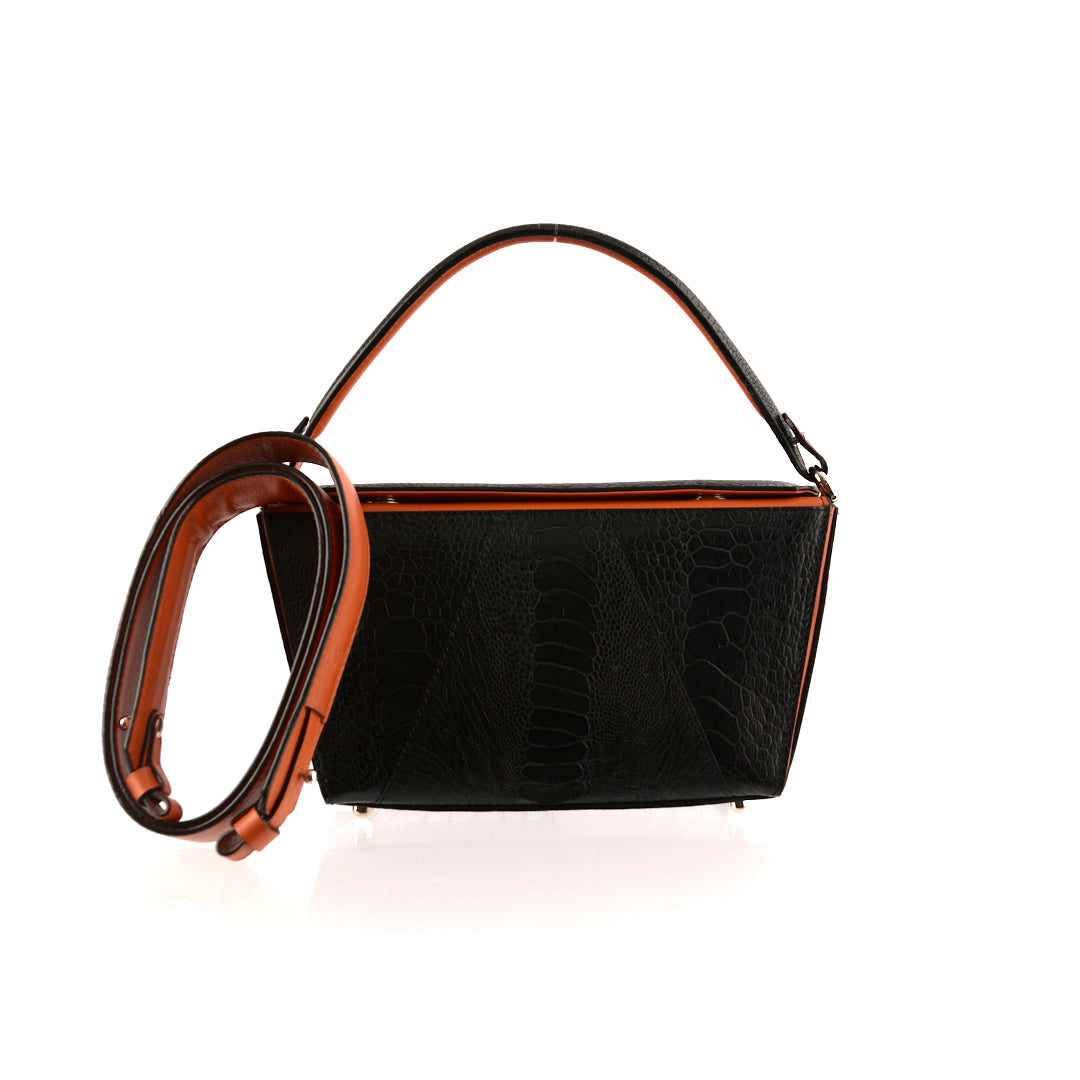 A black handbag with orange gussets and a removable brown strap, featuring a sleek and minimalistic design.