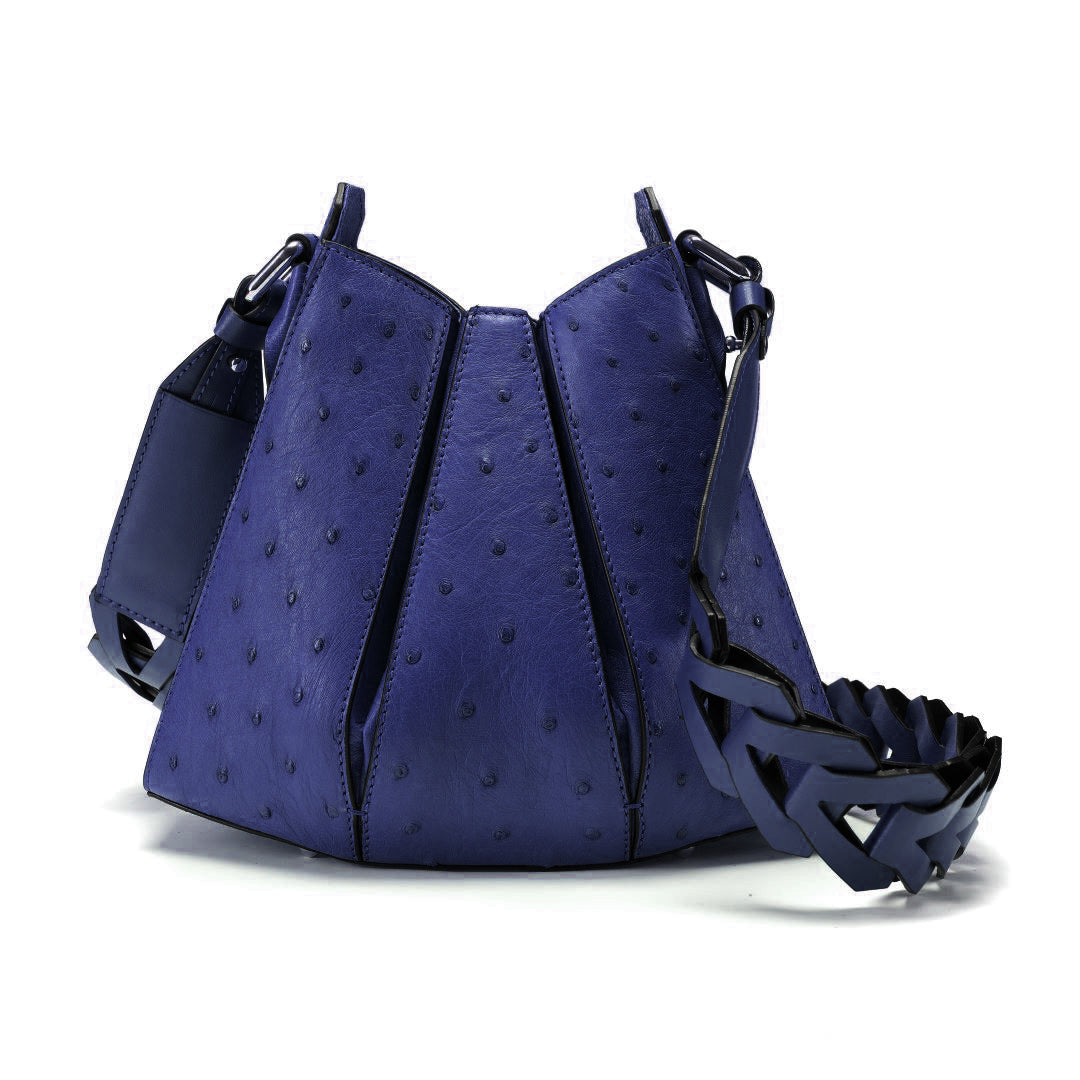 A blue ostrich-textured leather shoulder bag with a wide woven leather strap, displayed on a clean white background.